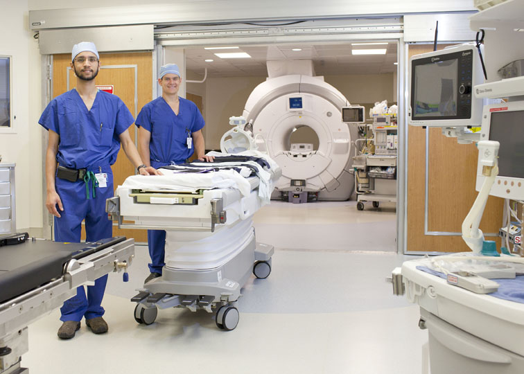 Our intraoperative MR Suite as seen from the OR section and looking through open doors to the magnet room. Our two former chief residents, Ben Miranpuri and Brandon Rocque (front to back), are standing aside the patient transfer table positioned just behind the OR table.